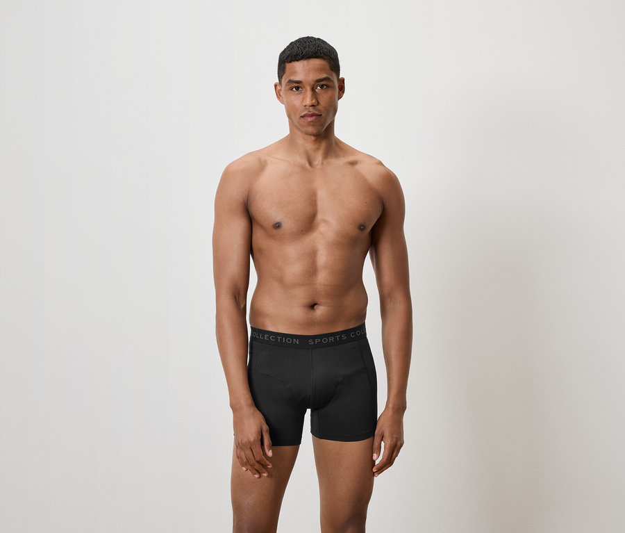 Mann ohne Hemd posiert in schwarzen Boxershorts.