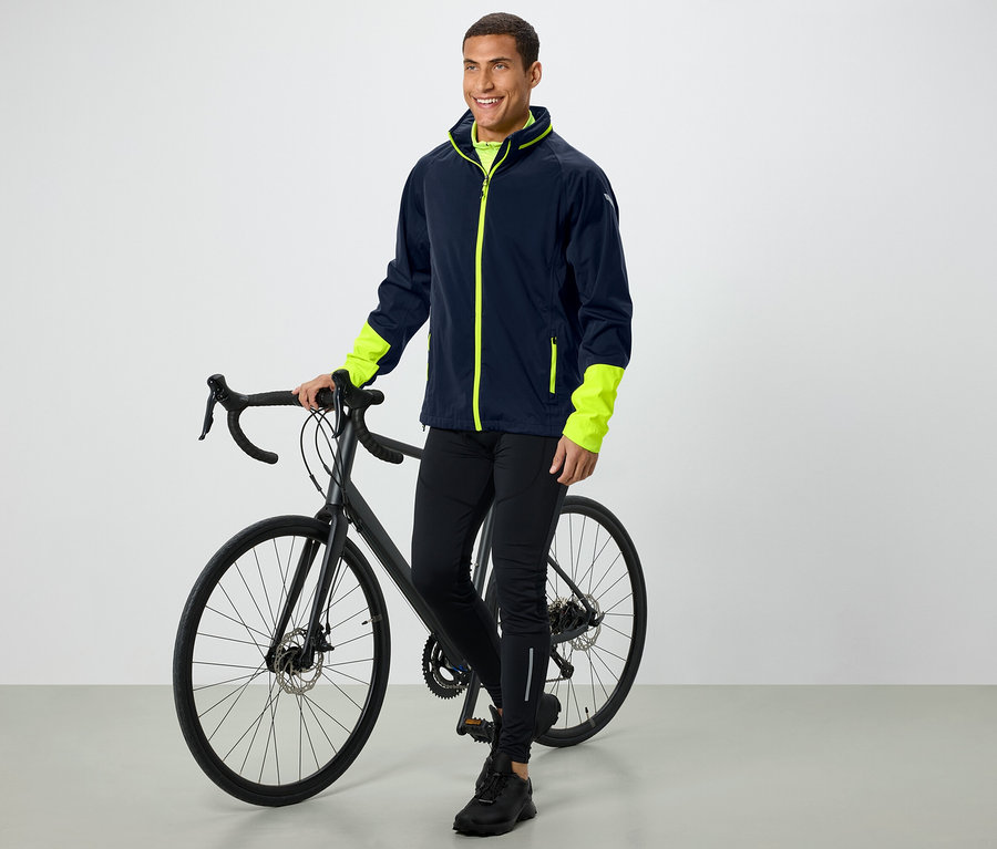 Ein Mann steht neben einem Fahrrad und trägt eine Jacke mit neonfarbenen Ärmeln.