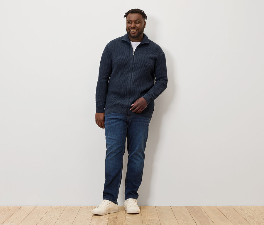 Mann steht und trägt eine Strickjacke, navy meliert, Jeans und Turnschuhe.