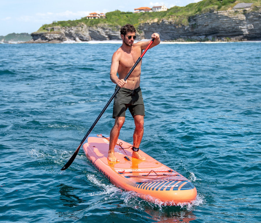 Mann paddelt auf einem orangefarbenen Aqua Marina SUP Board »Monster« 12'0" auf dem Meer.