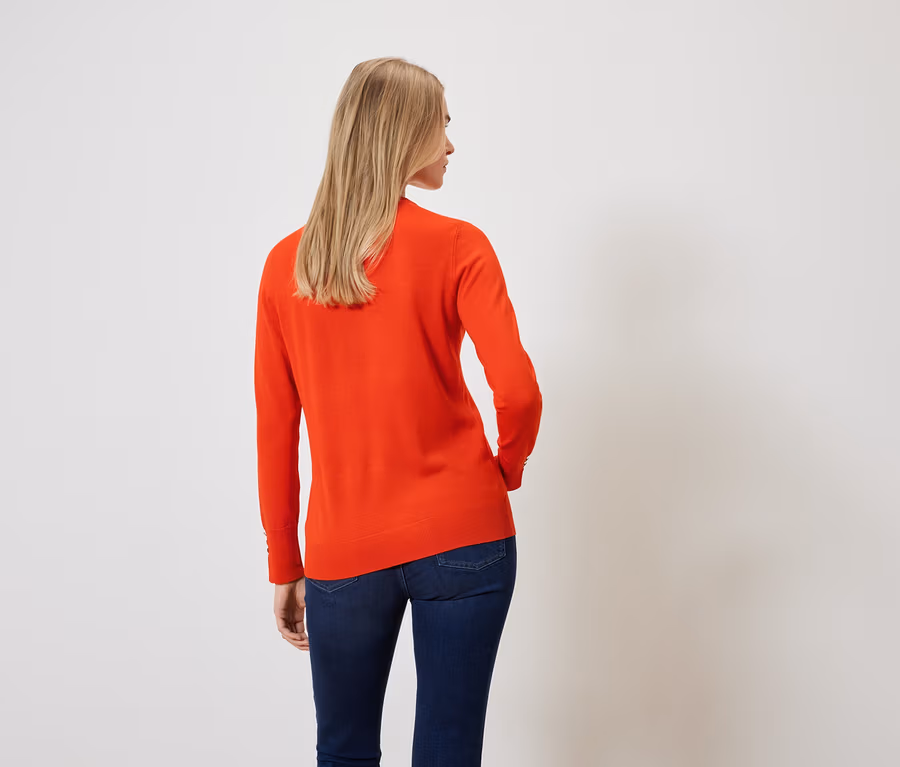 Rückansicht einer blonden Frau in orangefarbenem Pullover und dunkelblauen Jeans.