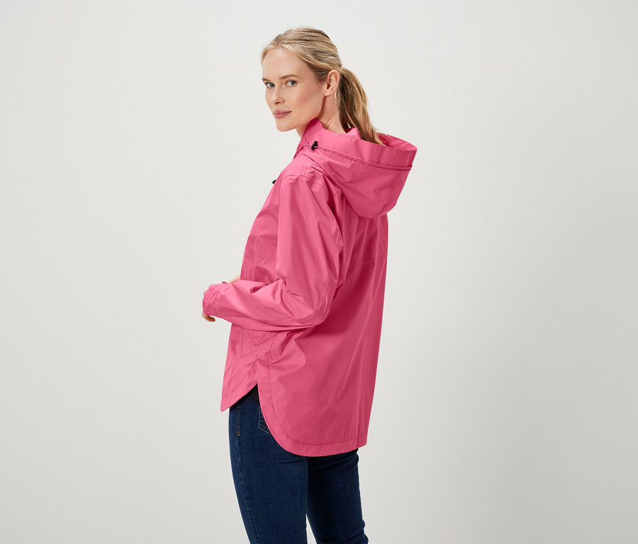 Frau blickt über die Schulter und trägt eine pinke Jacke und Jeans.