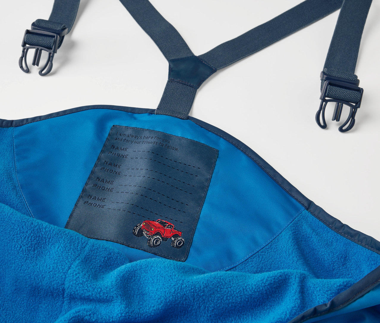 Detailaufnahme einer blauen Kinder-Thermo-Regenhose mit Trägern und einem roten Autoaufnäher.