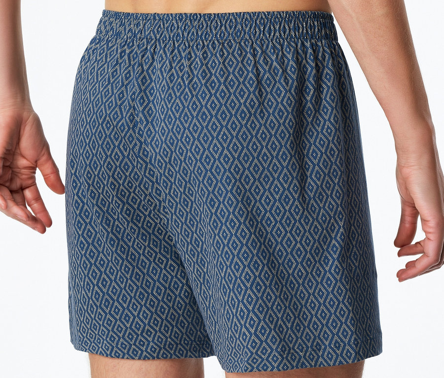 Ein Mann trägt blaue SCHIESSER Jersey-Boxer mit Rautenmuster und elastischem Bund.