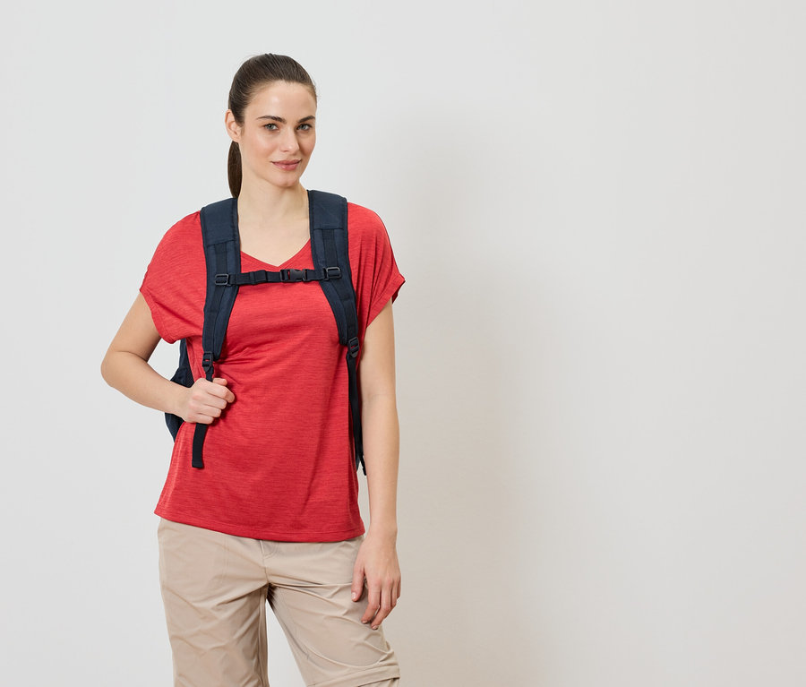 Frau trägt einen dunkelblauen Rucksack über einem roten T-Shirt und beigen Hosen.