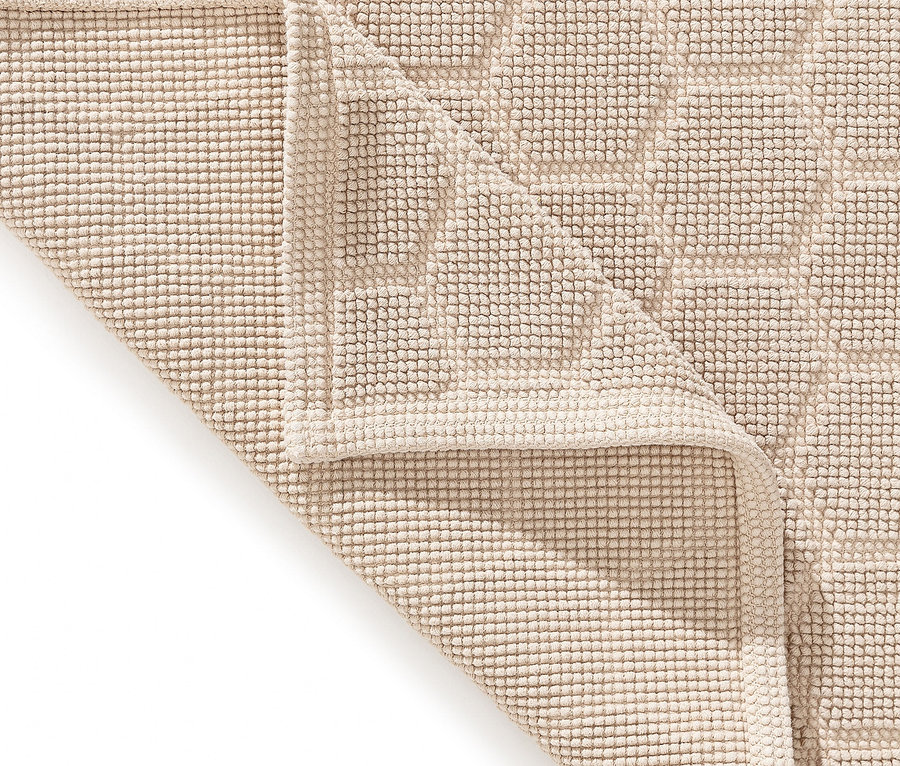 Nahaufnahme eines beigen Badvorlegers mit hochfloriger Textur und geometrischem Muster, wobei eine Ecke umgeschlagen ist.