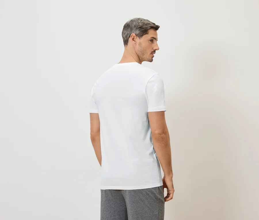 Mann von hinten in weißem T-Shirt und grauer Hose vor weißem Hintergrund.