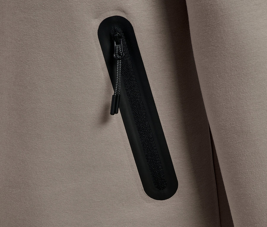 Nahaufnahme einer graubeigen Jacke mit einer schwarzen Reißverschlusstasche.