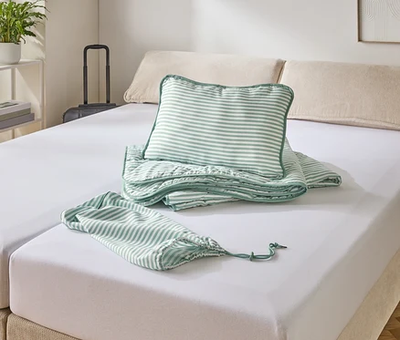 Ein Bett mit weißem Spannbettlaken, darauf ein gestreiftes Kissen, eine Decke und ein Beutel.
