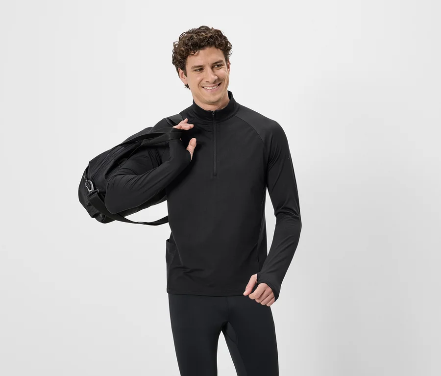 Mann mit lockigem Haar in schwarzem Sportoberteil mit Reißverschluss und schwarzer Hose, mit schwarzer Sporttasche über der Schulter.