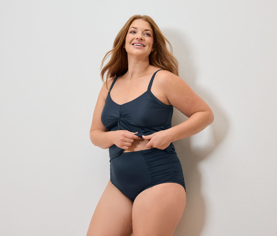 Frau mit langen roten Haaren, die einen marineblauen Badeanzug trägt und lächelt.