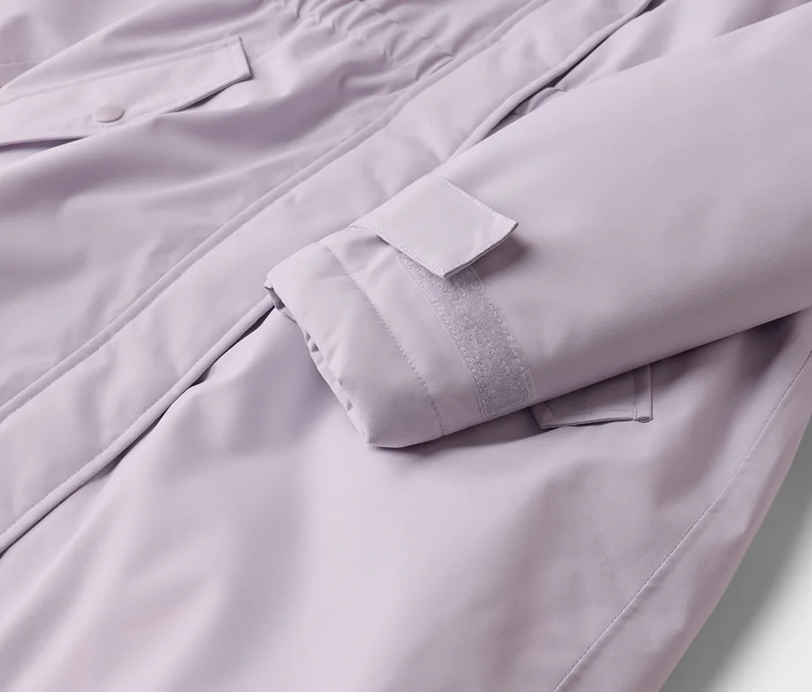 Nahaufnahme einer lila Jacke, die einen Ärmel mit verstellbarer Klettverschlussmanschette und eine Pattentasche mit Knopfverschluss zeigt.