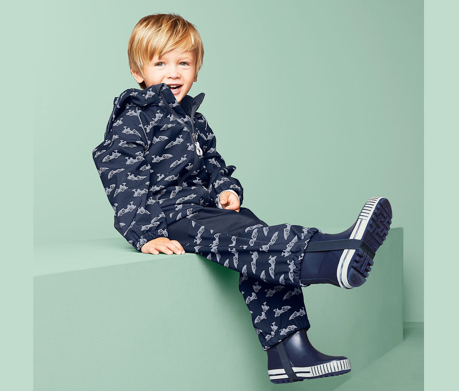 Junge sitzt in blauem Softshell-Overall mit Muster.