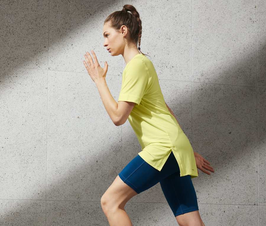 Frau im Laufschritt trägt ein Longshirt, blaue Shorts und Turnschuhe.