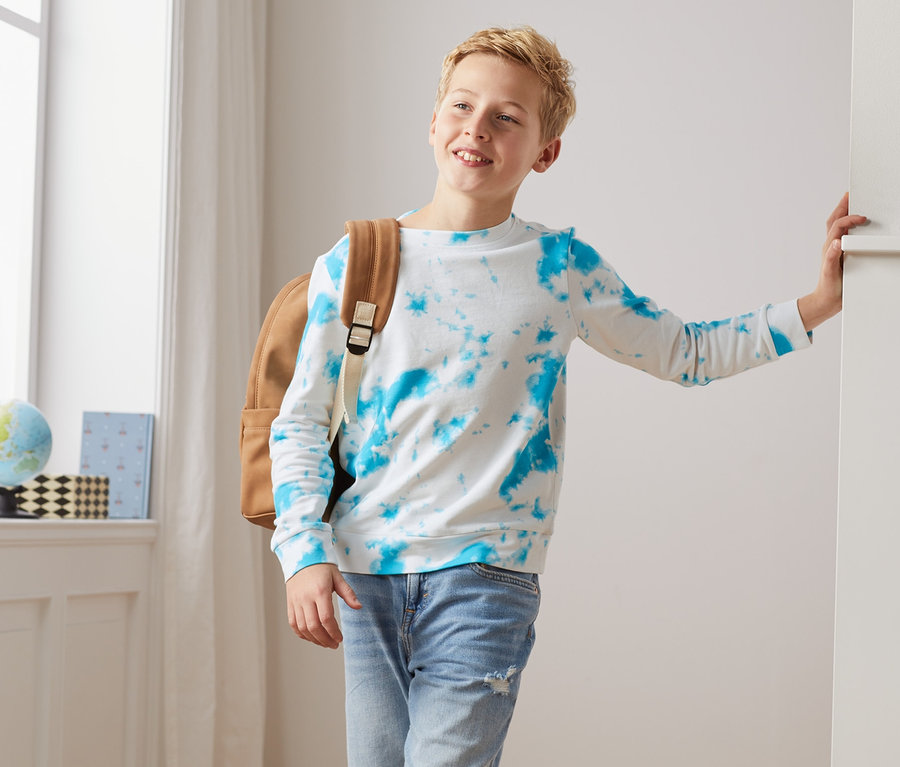 Junge mit braunem Rucksack trägt ein Sweatshirt.