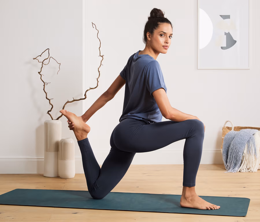 Frau in blauer Sportbekleidung dehnt sich auf einer Matte. Sie trägt eine Sporttight.