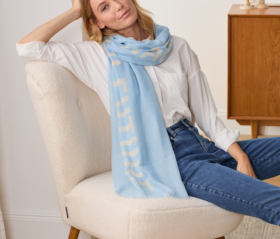 Frau sitzt im Sessel, trägt einen Webschal mit Statement-Print.