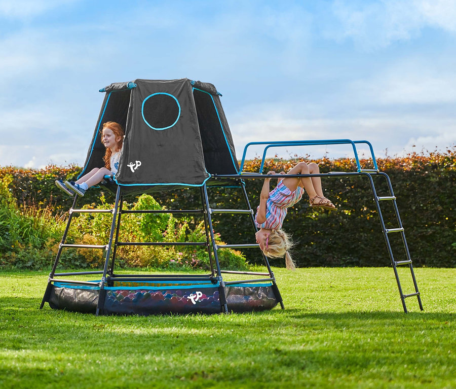 Zwei Mädchen spielen auf dem Kletterturm »Explorer« mit Zelt auf einer Wiese.