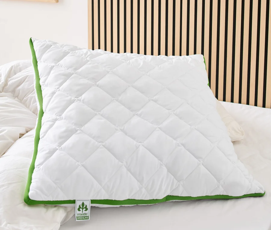 Ein weißes, gestepptes irisette® greenline Kopfkissen mit Klimaband und grüner Bordüre liegt auf einem Bett.