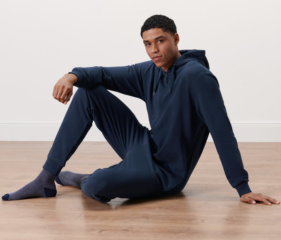 Mann sitzt in marineblauem Lounge-Overall auf dem Boden.