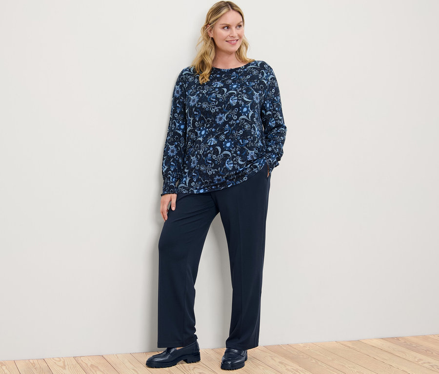 Frau posiert in einem bedruckten Blusenshirt und einer Komfort-Jerseyhose.