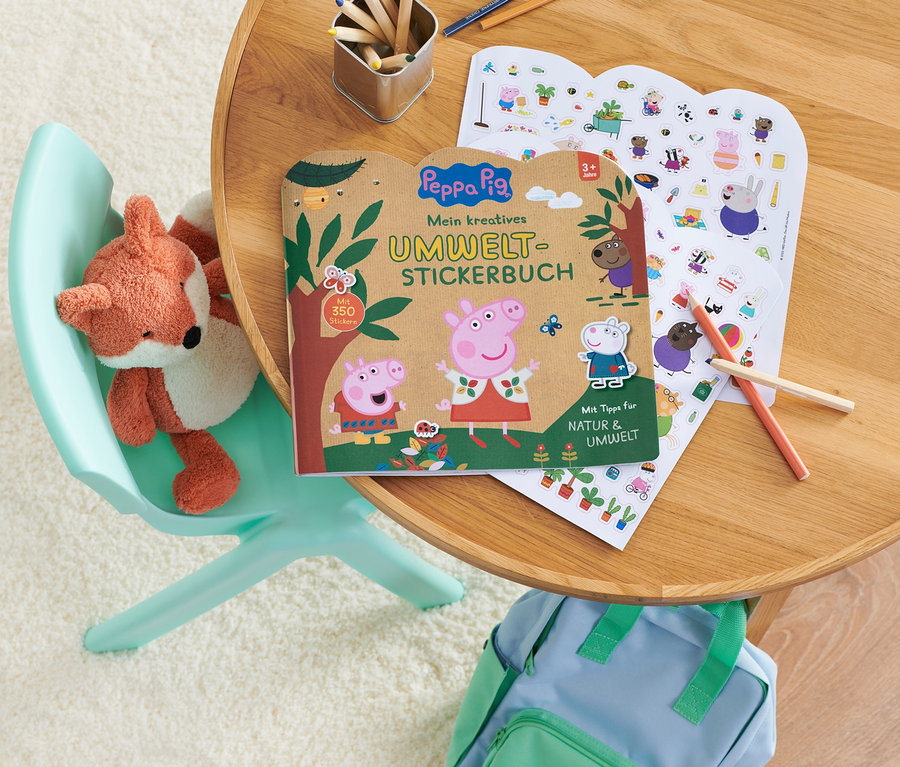 Auf einem Tisch liegen ein »Peppa Pig ‒ mein kreatives Umwelt-Stickerbuch« und ein Bogen mit Aufklebern. Auf einem Stuhl sitzt ein Stofffuchs.