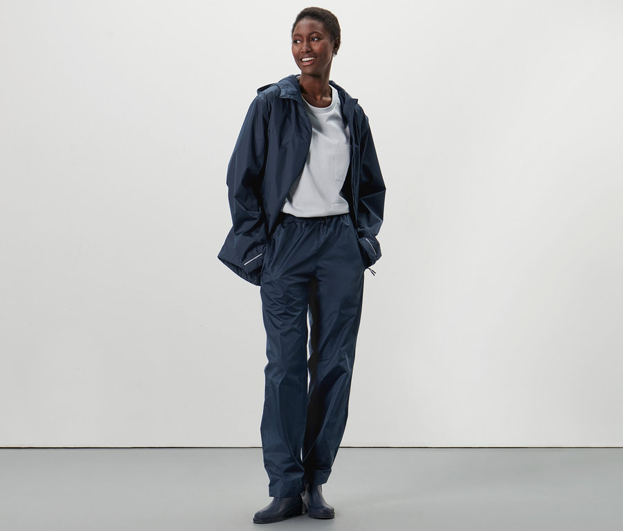 Eine Afroamerikanerin steht und trägt eine Unisex-Regenhose und eine Regenjacke.