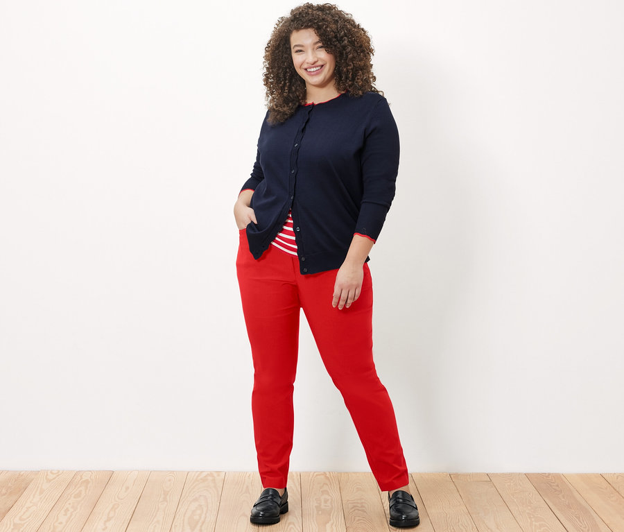 Frau posiert in roter Bengalin-Hose, einem gestreiften Shirt und einem Feinstrick-Cardigan mit Wellenkante.