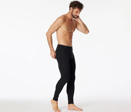 Mann, der eine schwarze SCHIESSER lange Unterhose mit Bio-Baumwolle trägt und sie an der Hüfte anpasst, während er nach unten blickt.