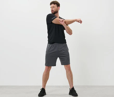 Mann dehnt Arm in Sportshorts.