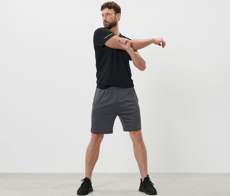 Mann dehnt Arm in Sportshorts.
