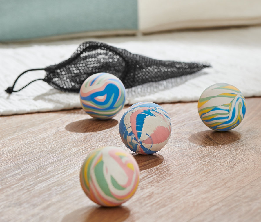 Vier mehrfarbige Flummis und eine schwarze Netztasche auf einem Holzboden.