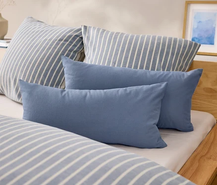 Auf einem Bett liegen zwei blaue, rechteckige Kissen und zwei Kissen mit blau-weißen Streifen.