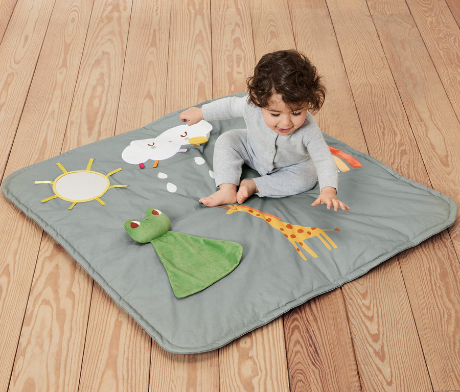 Baby sitzt auf Baby-Activity-Decke mit Sonne, Wolken, Giraffe und Frosch Motiven.