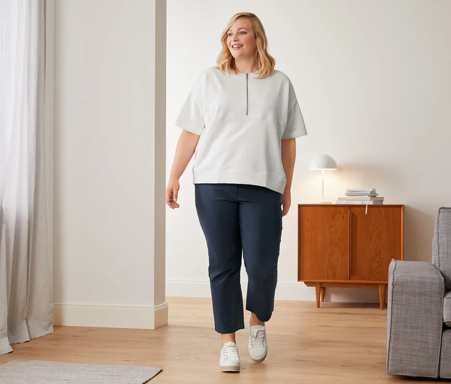 Eine Frau geht in weißen Canvas-Sneakern, einer weißen 7/8-Stretchhose und einem Oversized-Sweatshirt.