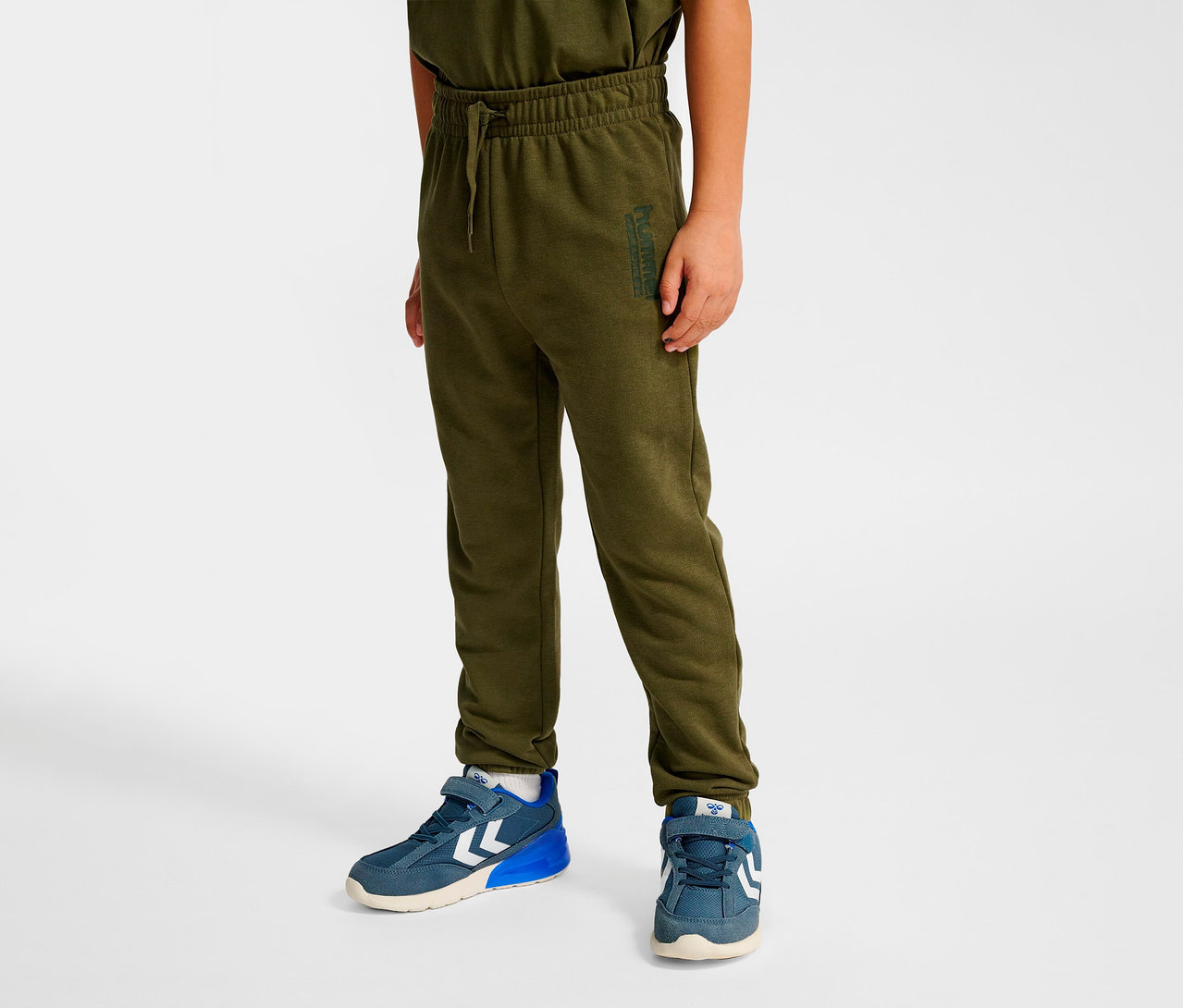 Junge trägt grüne HUMMEL HMLJR Base Regular Pants und blaue Schuhe.