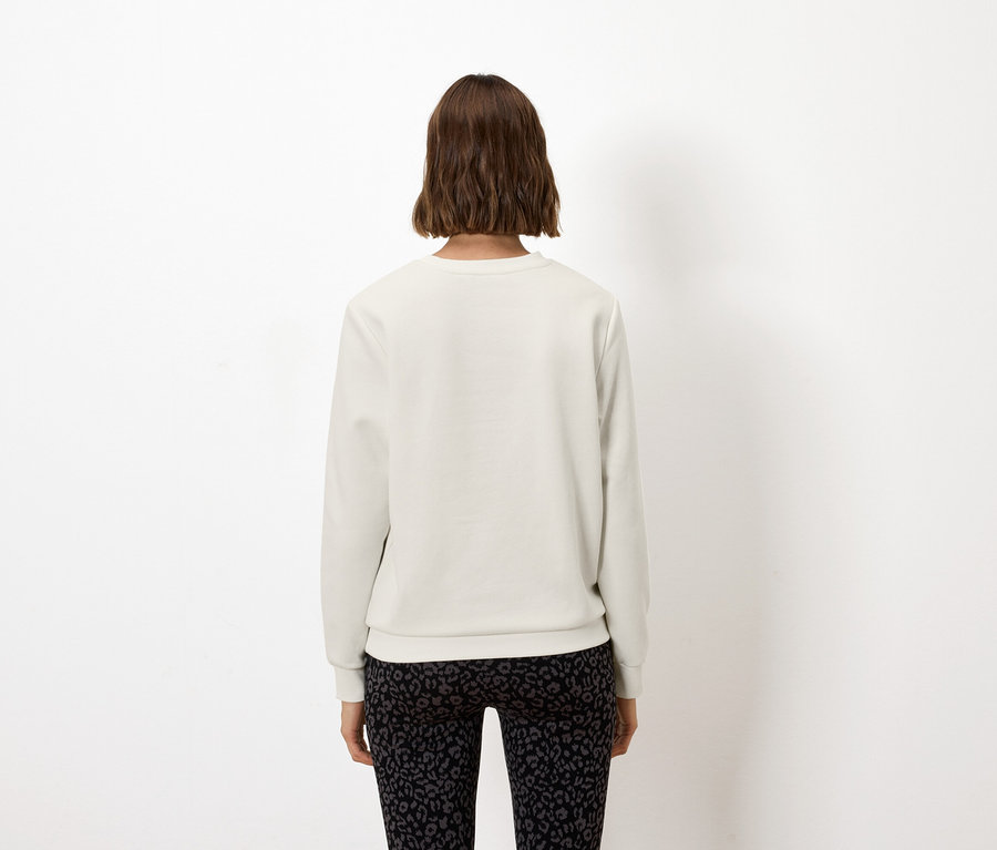 Eine Frau steht von hinten und trägt ein weißes Sweatshirt und schwarze Leggings.