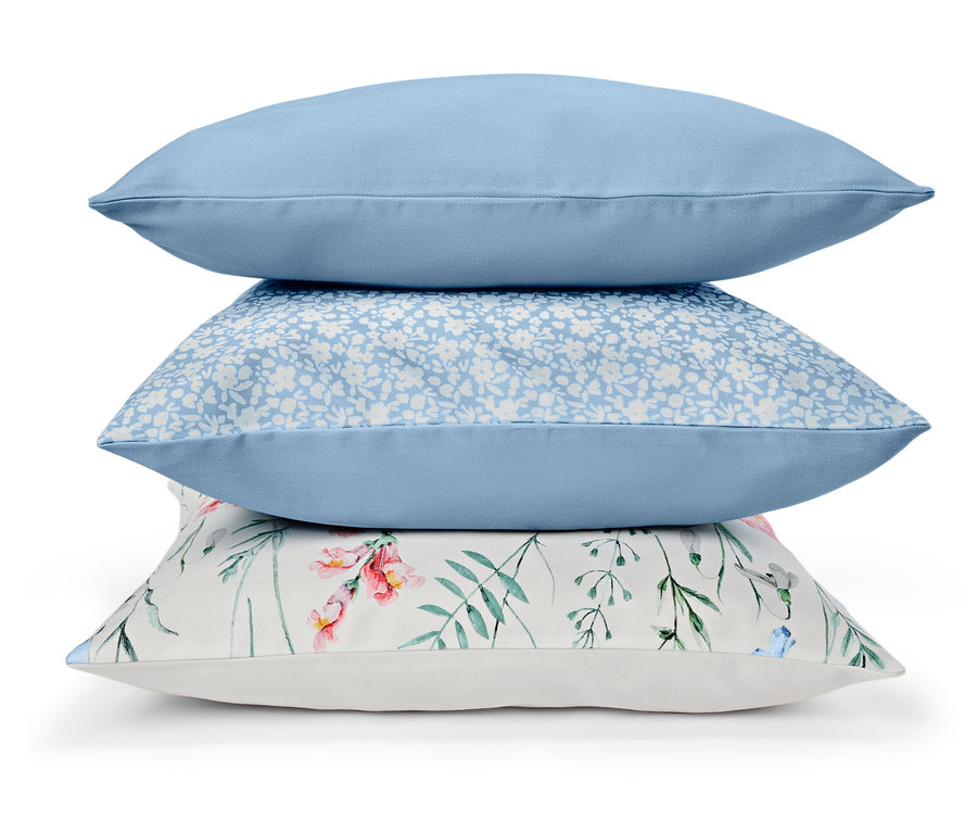 Drei Kissen sind gestapelt: einfarbig blau, blau mit weißen Blumen und weiß mit Blumenmuster.
