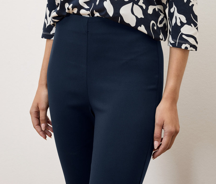 Nahaufnahme einer Frau, die marineblaue Hosen und ein Oberteil mit Blumenmuster trägt.