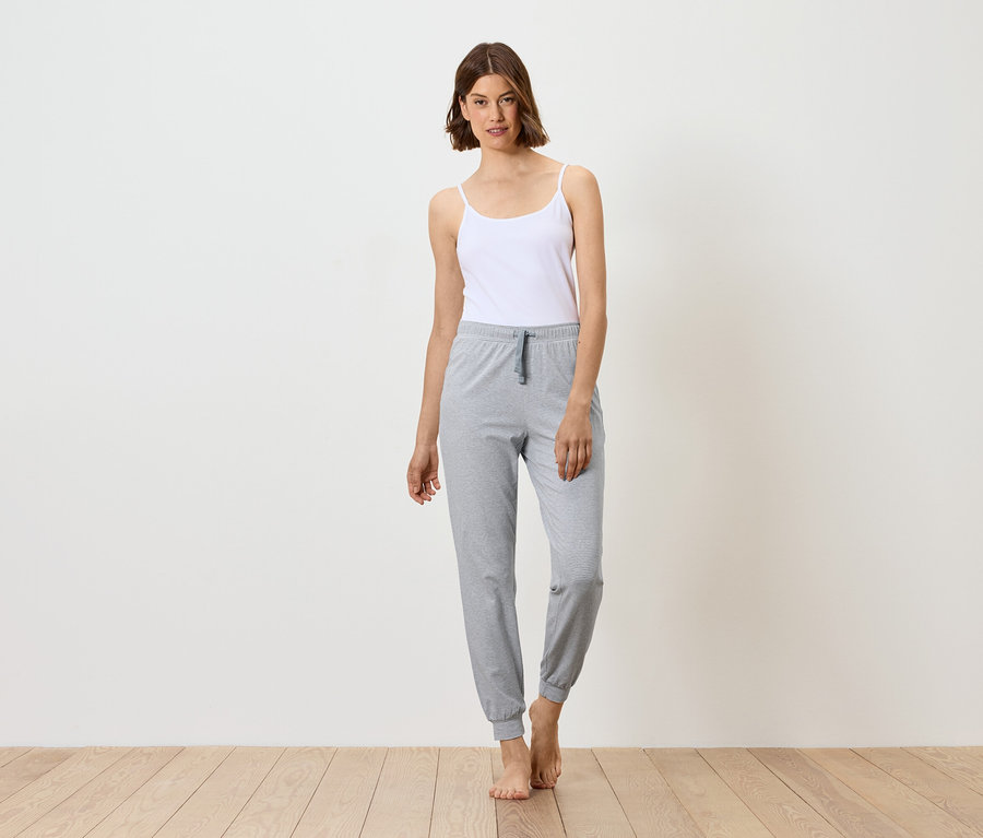 Frau steht barfuß in weißem Top und grauer Jogginghose.
