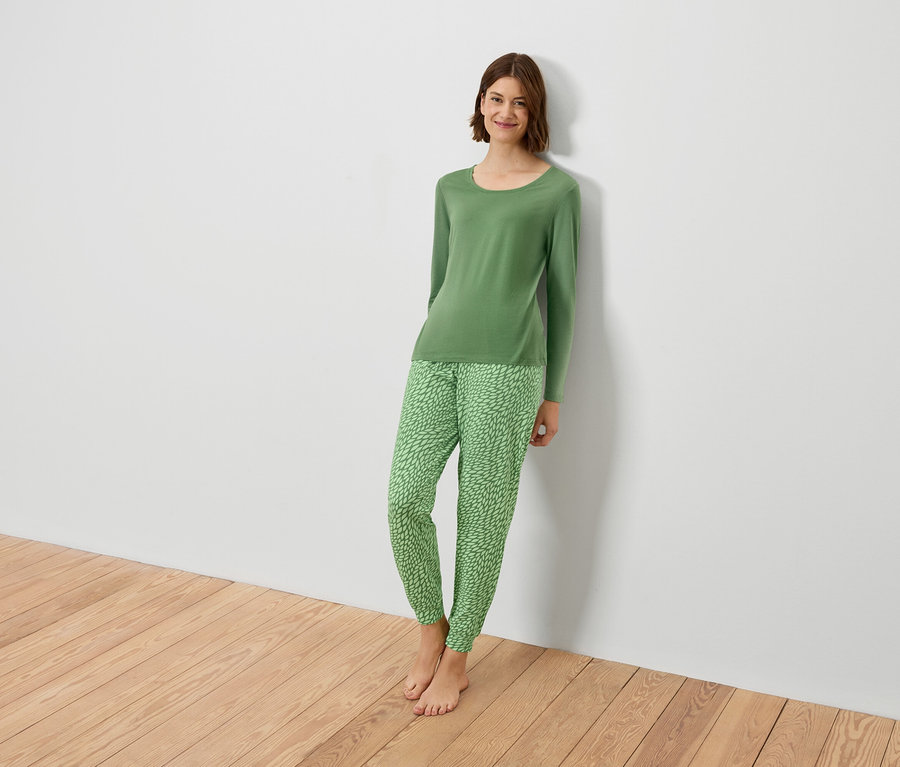 Frau im grünen Pyjama lehnt an einer weißen Wand.