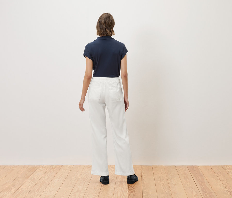 Frau steht mit dem Rücken, trägt ein dunkelblaues Poloshirt und weiße Hosen.