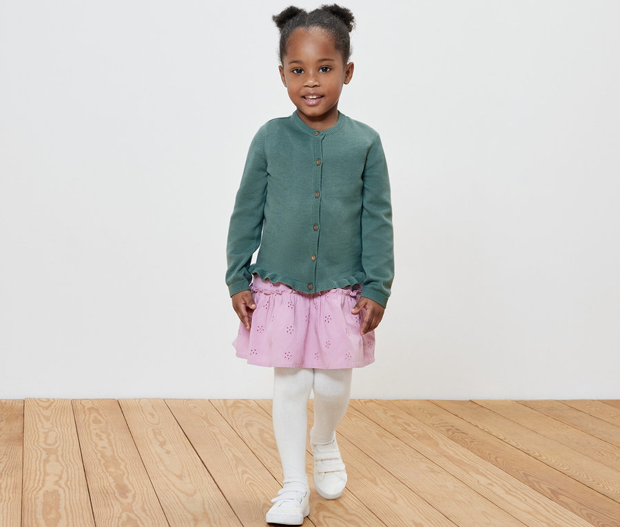 Lächelndes Mädchen posiert in Kinder-Strickjacke.