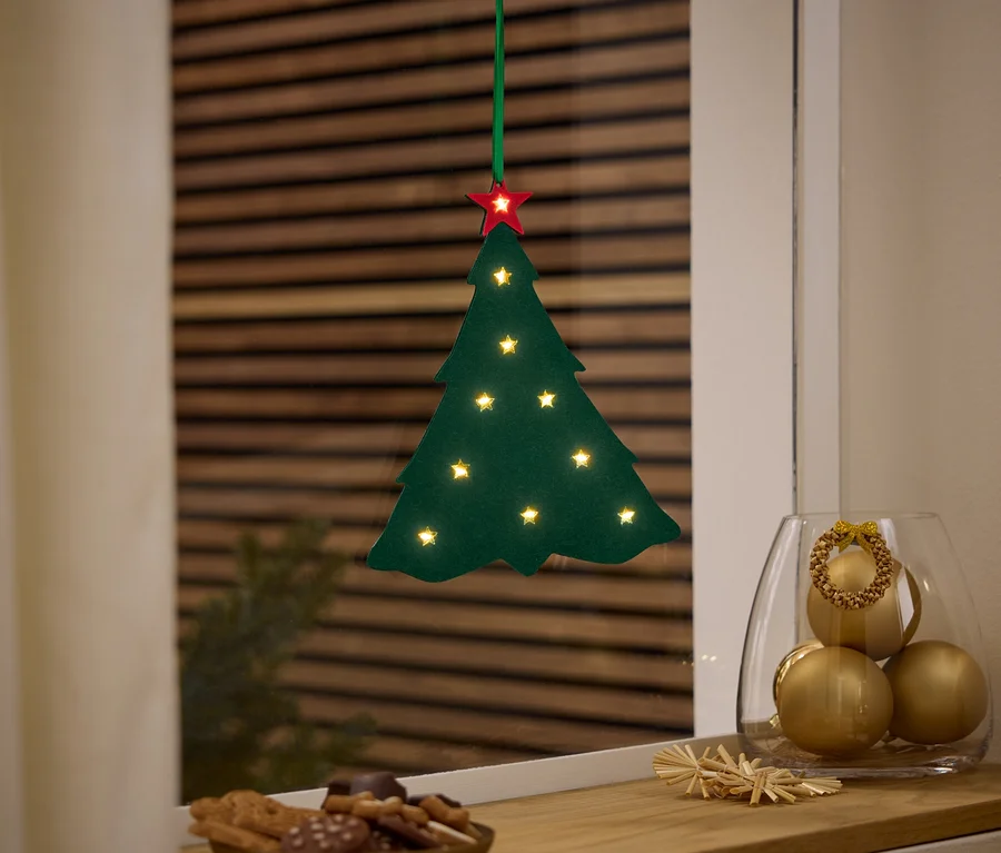Ein grüner Weihnachtsbaum mit einem roten Stern hängt am Fenster, neben einer Vase mit goldenen Ornamenten und einem Teller mit Süßigkeiten.