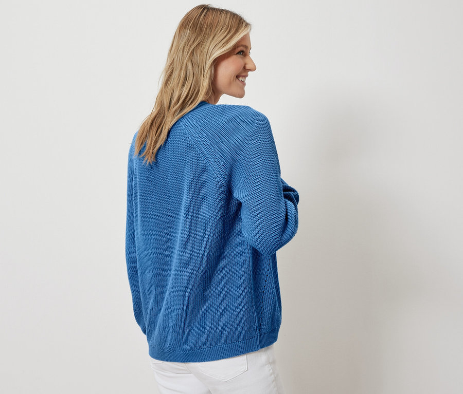 Frau posiert in offenem Cardigan und weißen Jeans.