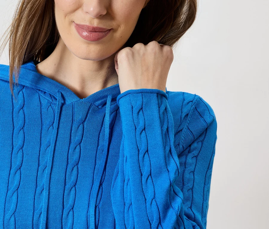 Nahaufnahme einer Frau mit blauem Strickpullover mit Kapuze und Zopfmuster.