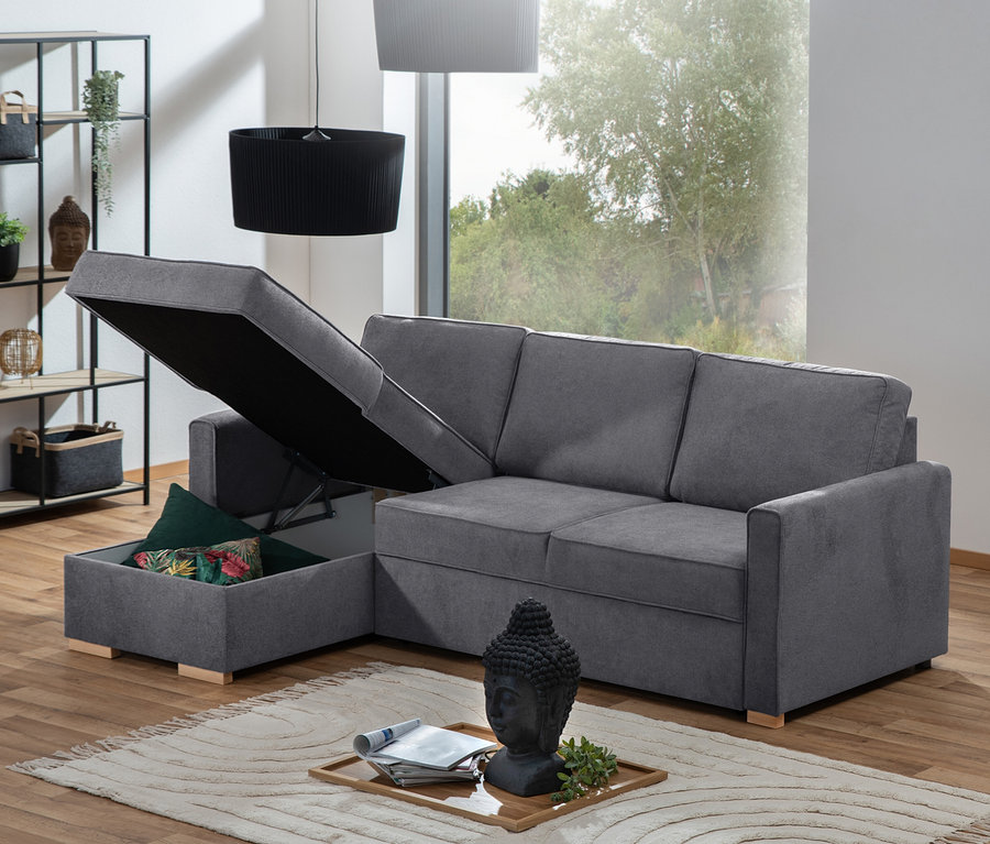 Graues Ecksofa »NovaLounge« mit ausgezogenem Bettkasten und Kissen auf einem Teppich.