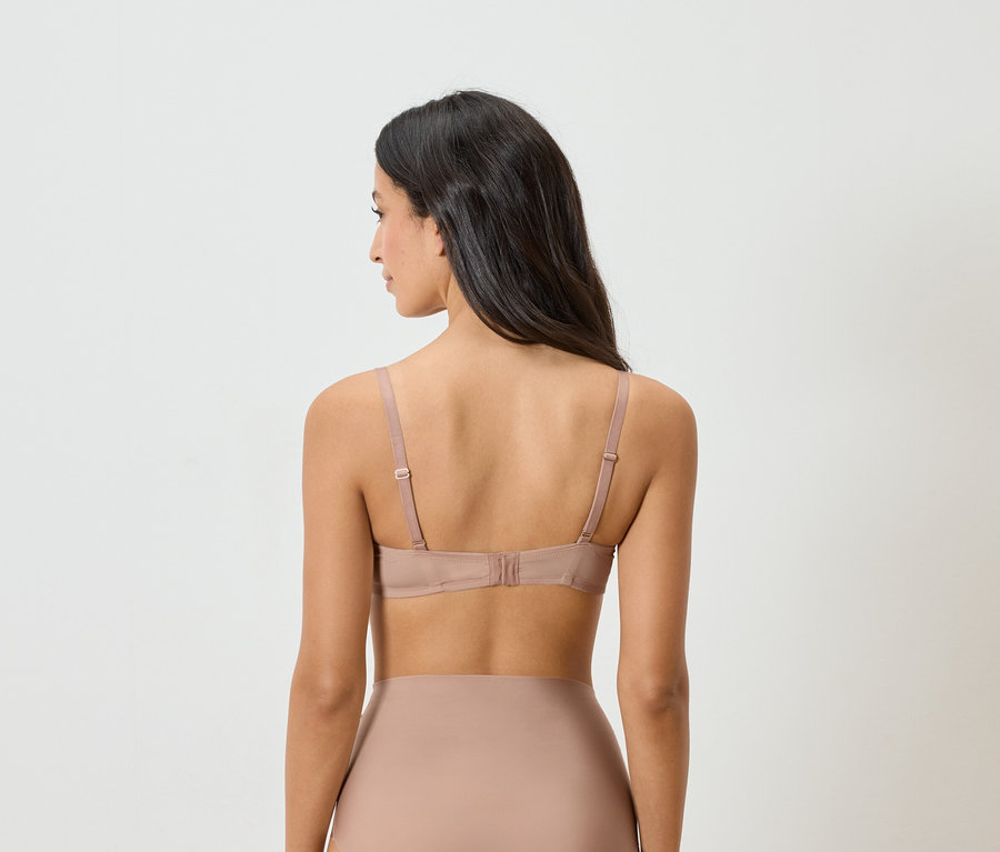 Rückansicht einer Frau mit dunklen Haaren, die einen nudefarbenen BH und Unterwäsche trägt.