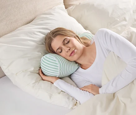 Eine Frau schläft in einem Bett mit einem gestreiften, zylindrischen Kissen unter ihrem Kopf.