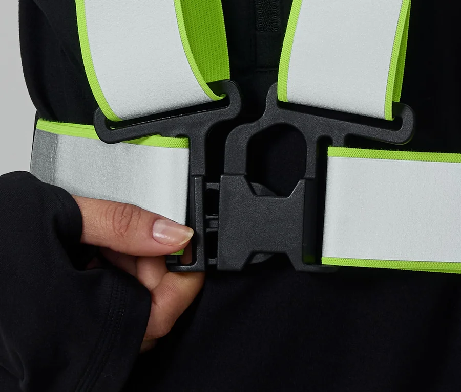 Hand schließt schwarzen Clip eines reflektierenden Sicherheitsgurtes mit neongrünen Rändern.